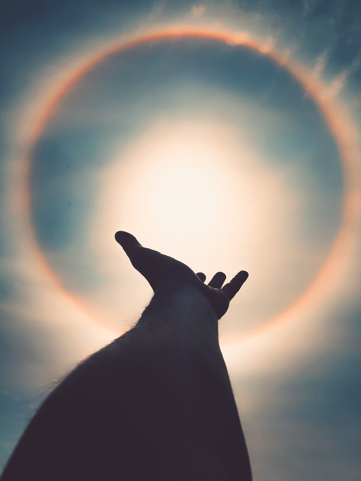 A hand reaching toward a halo of light around the sun