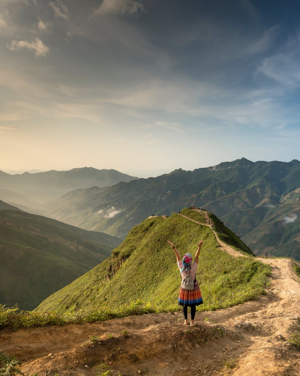 A person standing on a sunlit mountain ridge with arms raised